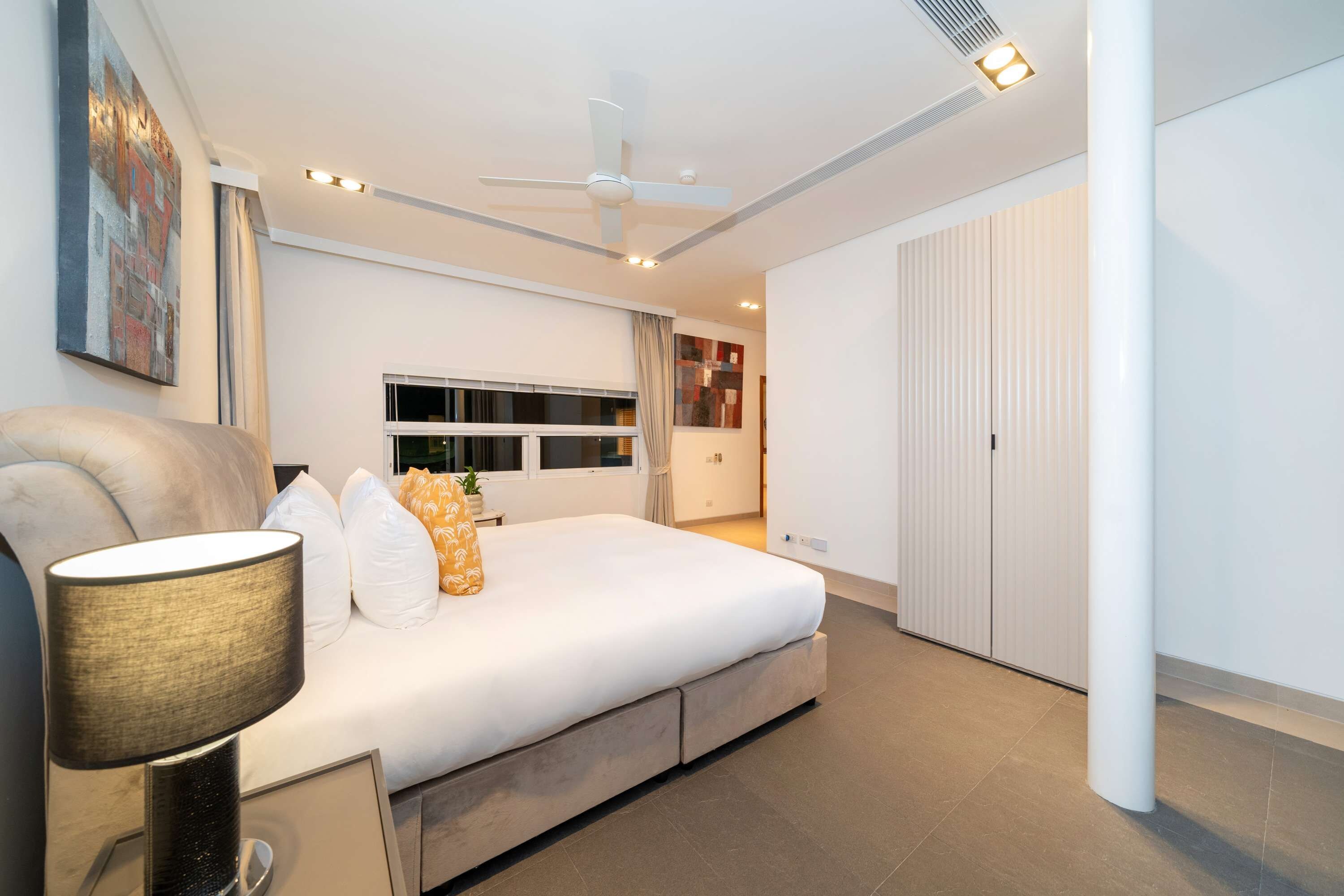 A modern bedroom with a large bed, a ceiling fan, and a nightstand with a lamp.