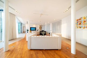 Una sala de estar moderna con un sofá blanco grande, un televisor de pantalla plana y un piano.