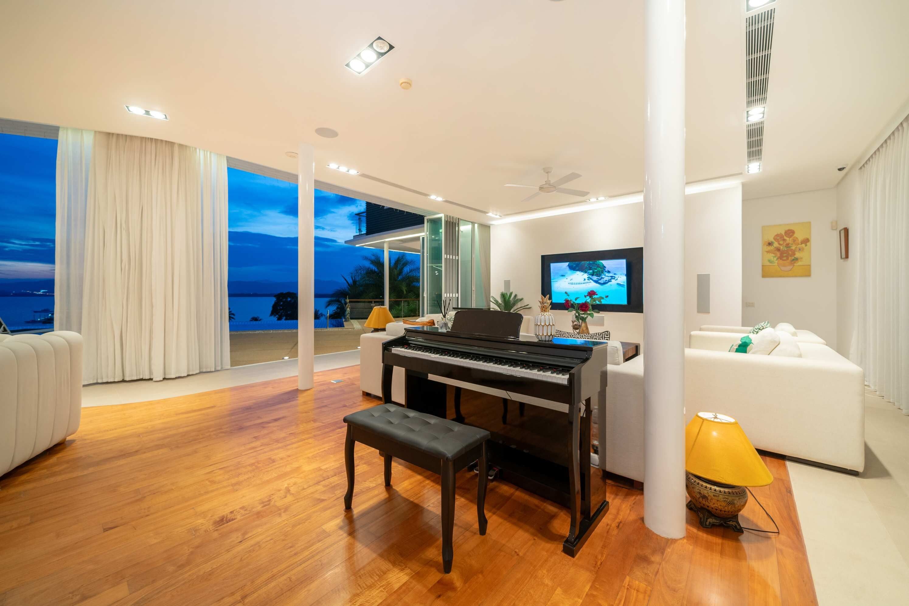 A modern living room with a piano, a television, and a view of the sea.