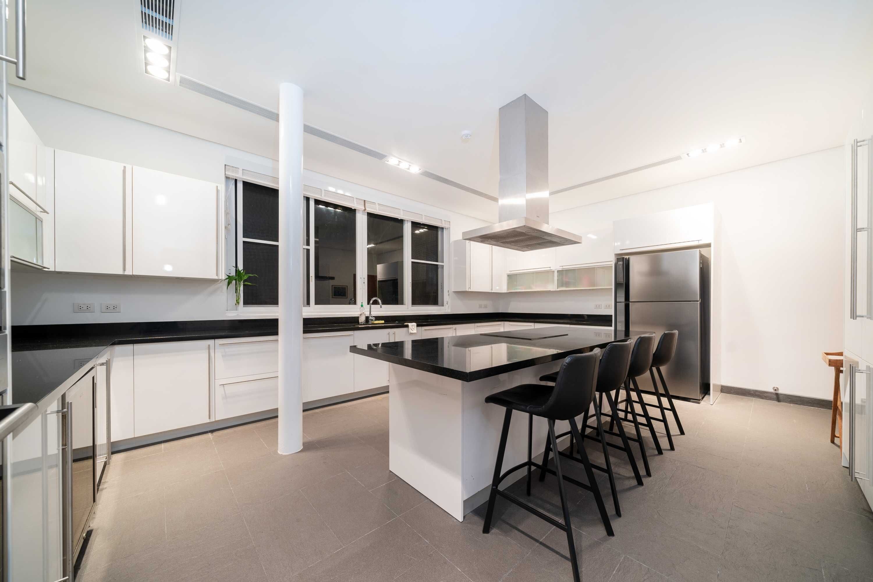 A modern kitchen with a central island, bar stools, stainless steel appliances, and white cabinetry.