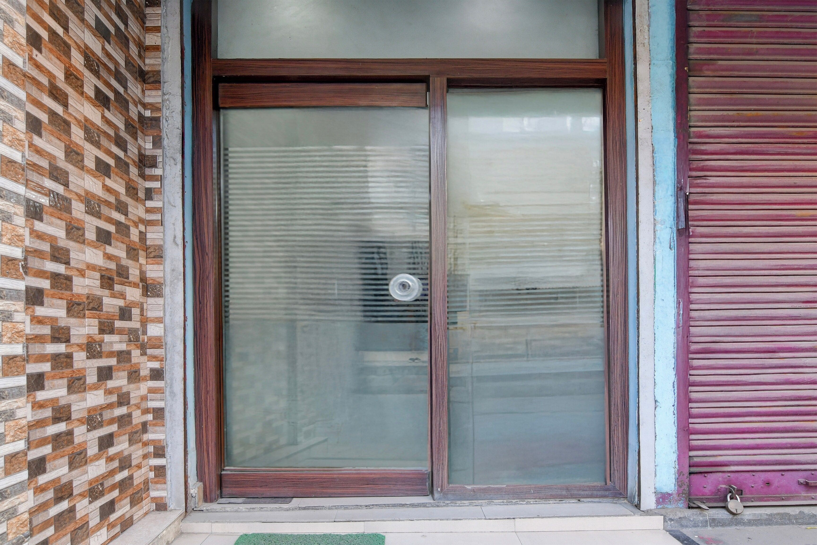 A closed glass door with a metal handle, a brick wall to the left, and a purple shutter to the right.