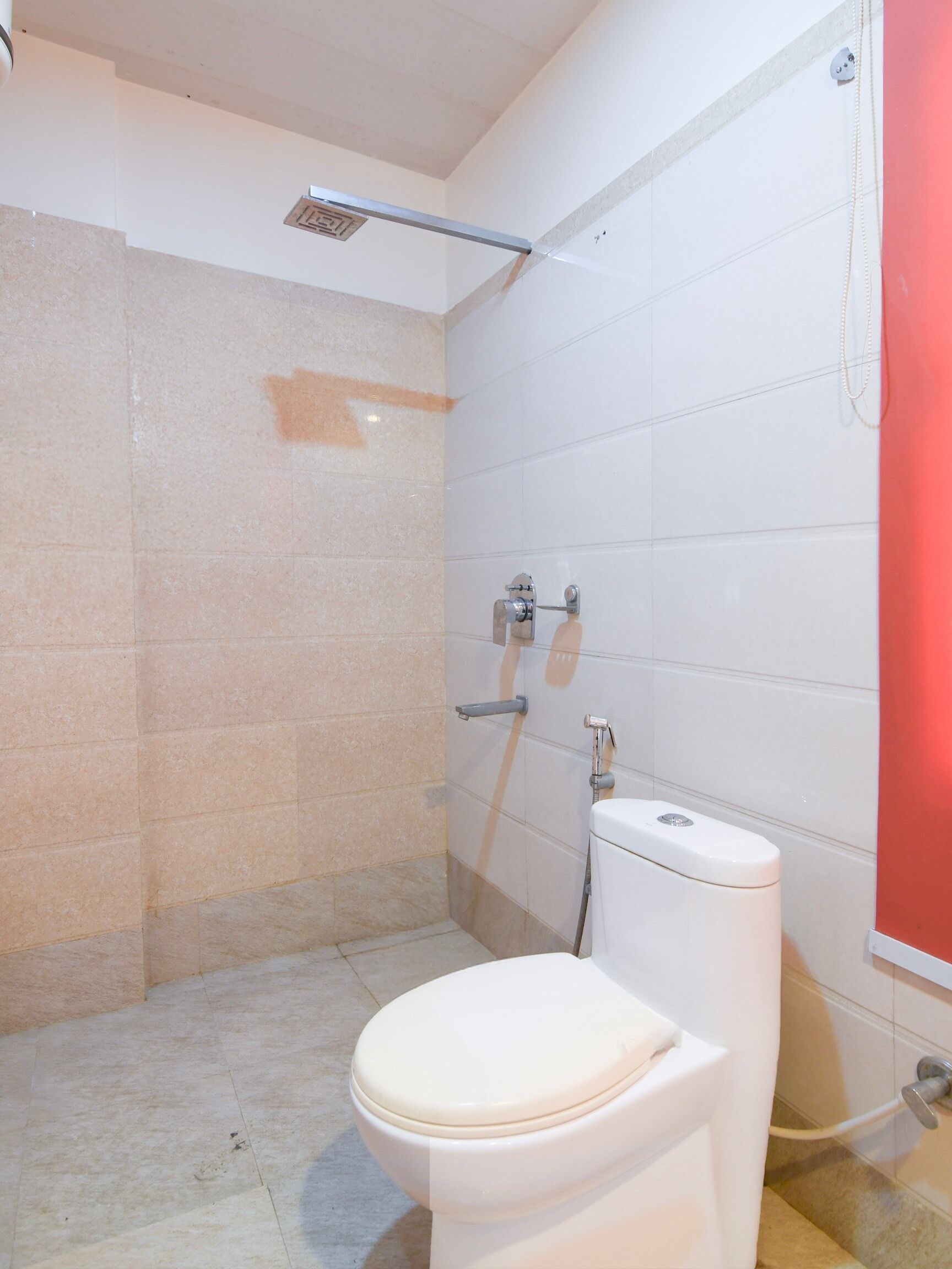 A small bathroom with a toilet, a shower area, and a red wall.