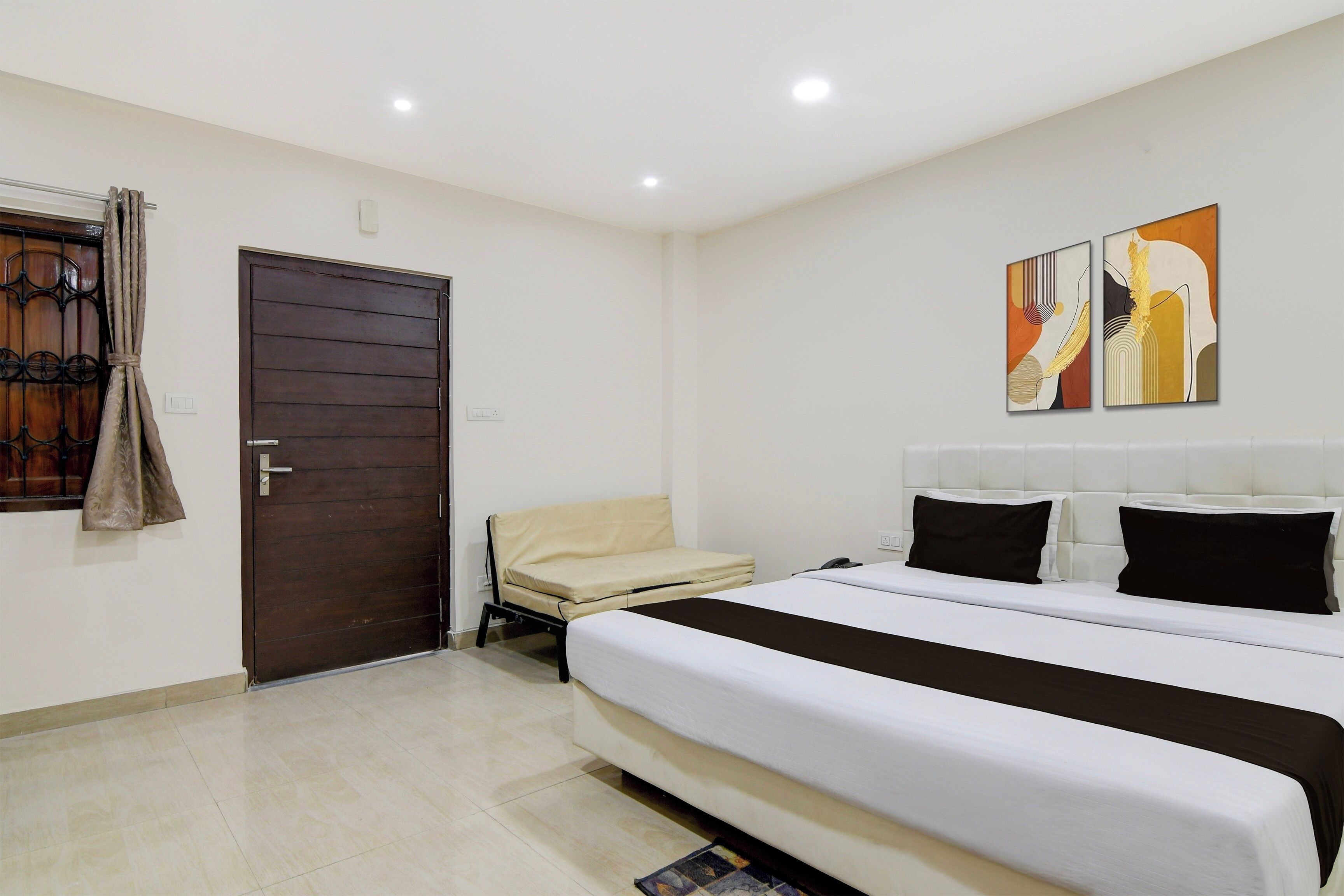 Habitación de hotel con cama, una silla, una puerta y dos obras de arte colgadas en la pared.