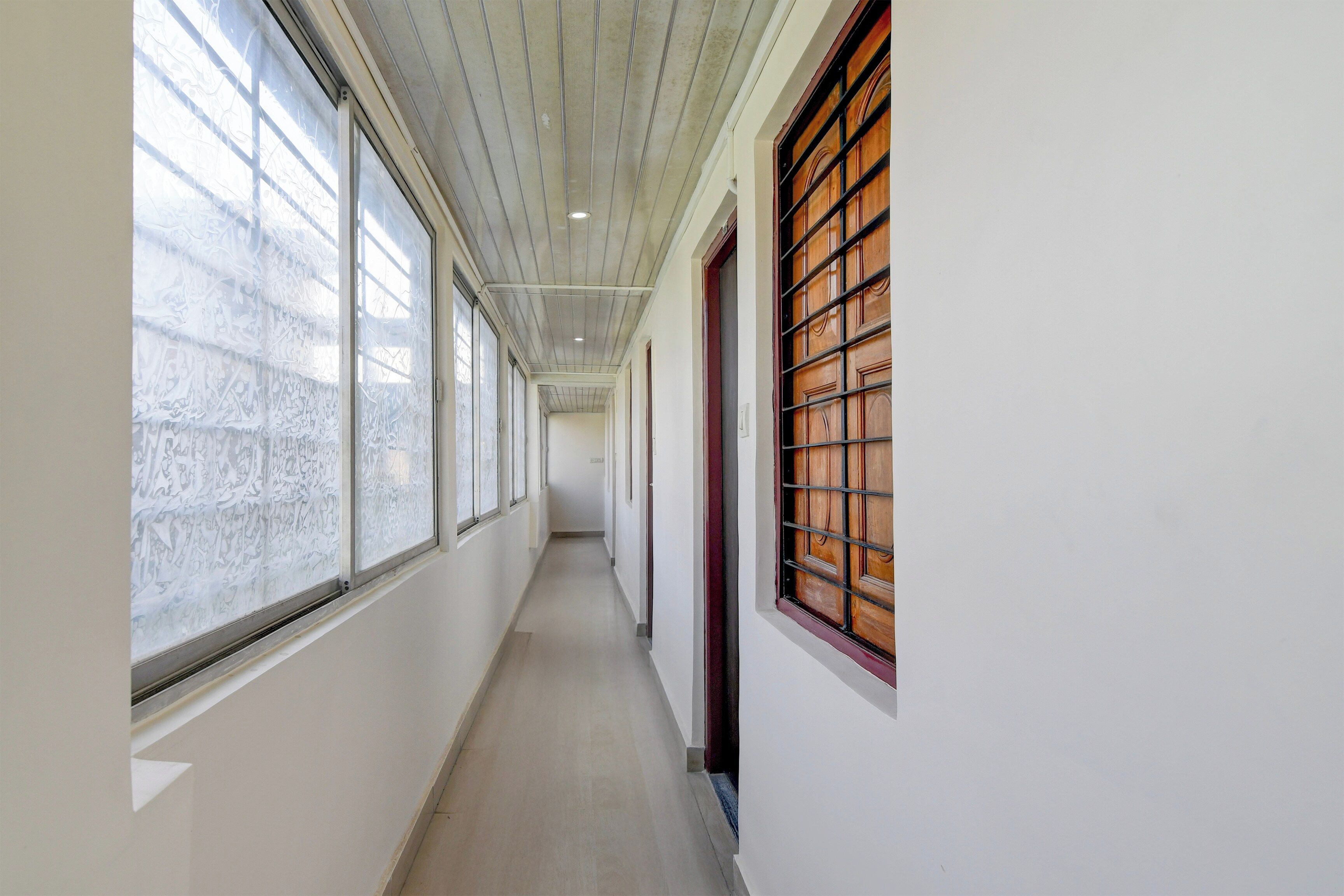 A corridor with large windows on one side and a wooden door on the other.