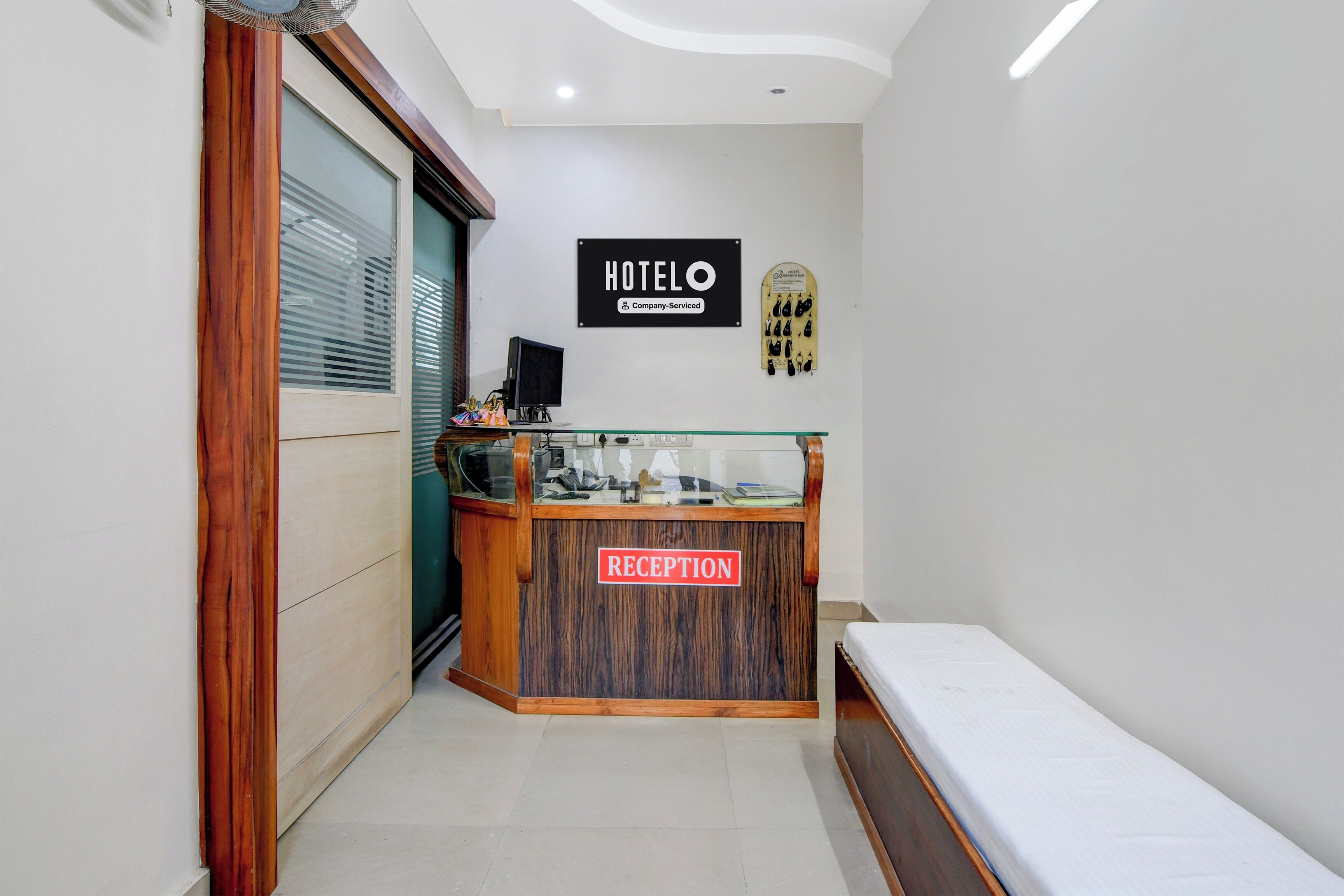 Zona de recepción de un hotel con mostrador, señal que indica que es un hotel de servicios empresariales y una cama en la esquina.