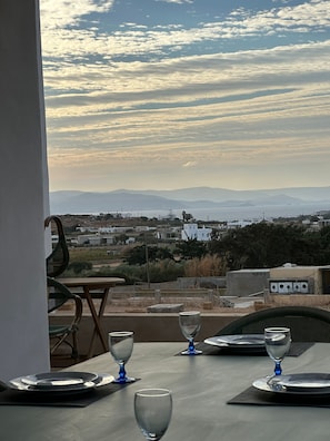 A table set for dining with a view of a coastal landscape and distant mountains. - Holiday Home 'The Pepper Tree Villa Swimming' with Sea View, Wi-Fi and Air Conditioning (Πάρος)