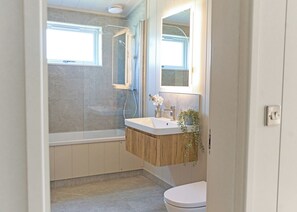 Une salle de bain moderne avec une douche à parois de verre, un meuble-lavabo en bois, des toilettes et un miroir au-dessus du lavabo.