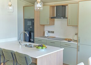 A modern kitchen with a central island, stainless steel sink, and a built-in oven. - Autograph Retreat Hot Tub 2 bed Luxury Lodge slps4 (Landford, Nr Salisbury)