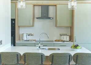 A modern kitchen with a central island, stainless steel appliances, and a built-in oven. - Autograph Retreat Hot Tub 2 bed Luxury Lodge slps4 (Landford, Nr Salisbury)