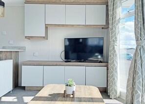 A modern living room with a flat-screen TV, built-in cabinets, a wooden coffee table, and a potted plant. - Gold 8 berth Pet Friendly (Chapel St Leonards)