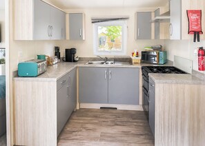 A compact kitchen with grey cabinets, a sink, a toaster, a coffee maker, and a fire blanket on the wall. - 2 bedroom accommodation in Colyton (Colyton)