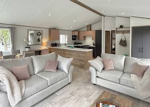 A modern living room with two grey sofas, a central island with a sink, and a kitchen area in the background. - Woodland 3 bed Lodge - Hazel (Notter Bridge, Saltash)