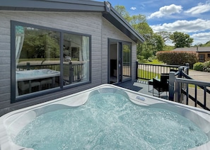 A modern house with a hot tub on the patio, large windows, and a deck. - Woodland 3 bed Lodge - Hazel (Notter Bridge, Saltash)