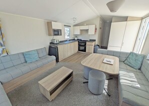 Een knus woongedeelte met een kitchenette, een bank, een eettafel en een klein bankje.