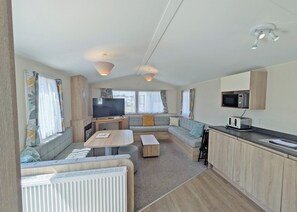 Ein kompakter Wohnbereich mit Sofa, Fernseher, einer kleinen Küche und einem Esstisch.