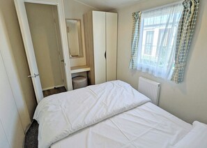 Ein Schlafzimmer mit Bett, Kleiderschrank, Heizkörper und einem Fenster mit Vorhängen.