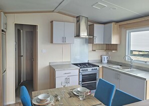 A compact kitchen with a stove, oven, and sink, and a dining area with a table set for two. - 1 bedroom accommodation in Dorchester (Dorchester)