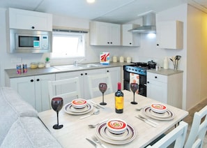 A modern kitchen with white cabinets, a microwave, a stove, and a dining table set for a meal. - 3 bedroom accommodation in Ettrick Valley, Nr Hawick (Ettrick Valley, Nr Hawick)