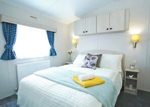 Een hotelkamer met een bed, een raam met gordijnen, een nachtkastje met een lamp en een wandkast.