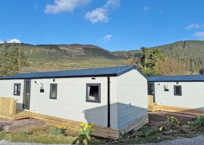 A row of mobile homes with a clear sky and a forested hill in the background. - 1 bedroom accommodation in Ettrick Valley, Nr Hawick (Ettrick Valley, Nr Hawick)