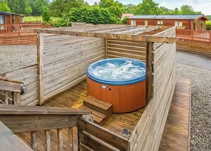 A hot tub surrounded by wooden deck areas with a view of a green landscape. - Modern two-bedroom holiday home. (Fort Augustus)