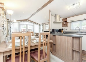 A modern kitchen with wooden cabinetry, a dining area with a table and chairs, and a large window providing natural light. - Modern two-bedroom holiday home. (Fort Augustus)