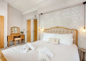 A hotel room with a large bed, a wooden dresser, a mirror, and a wall with decorative paneling. - 1 bedroom accommodation in Invermoriston (Invermoriston)