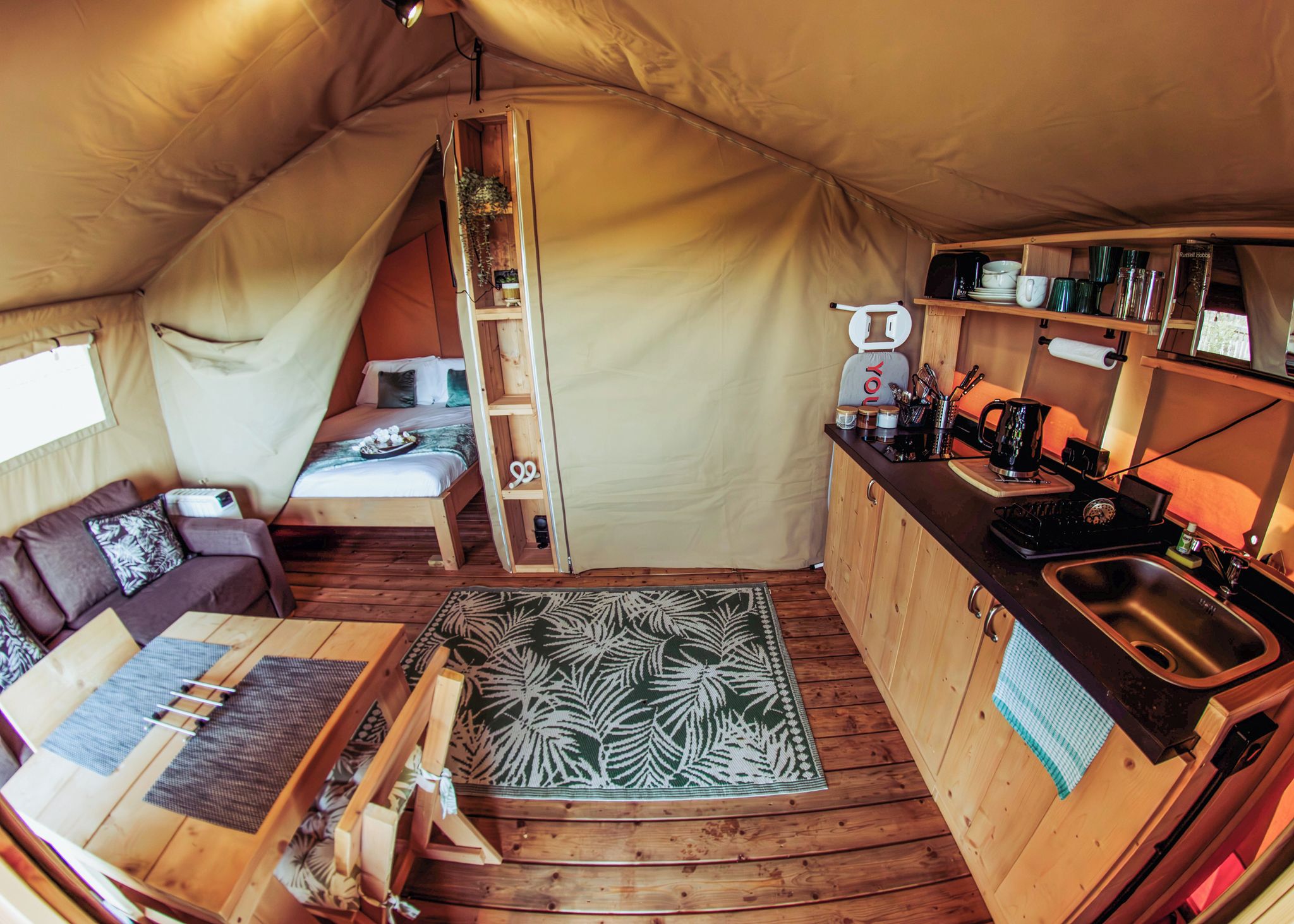 A cozy tent with a bed, a small kitchenette, and a seating area with a patterned rug.