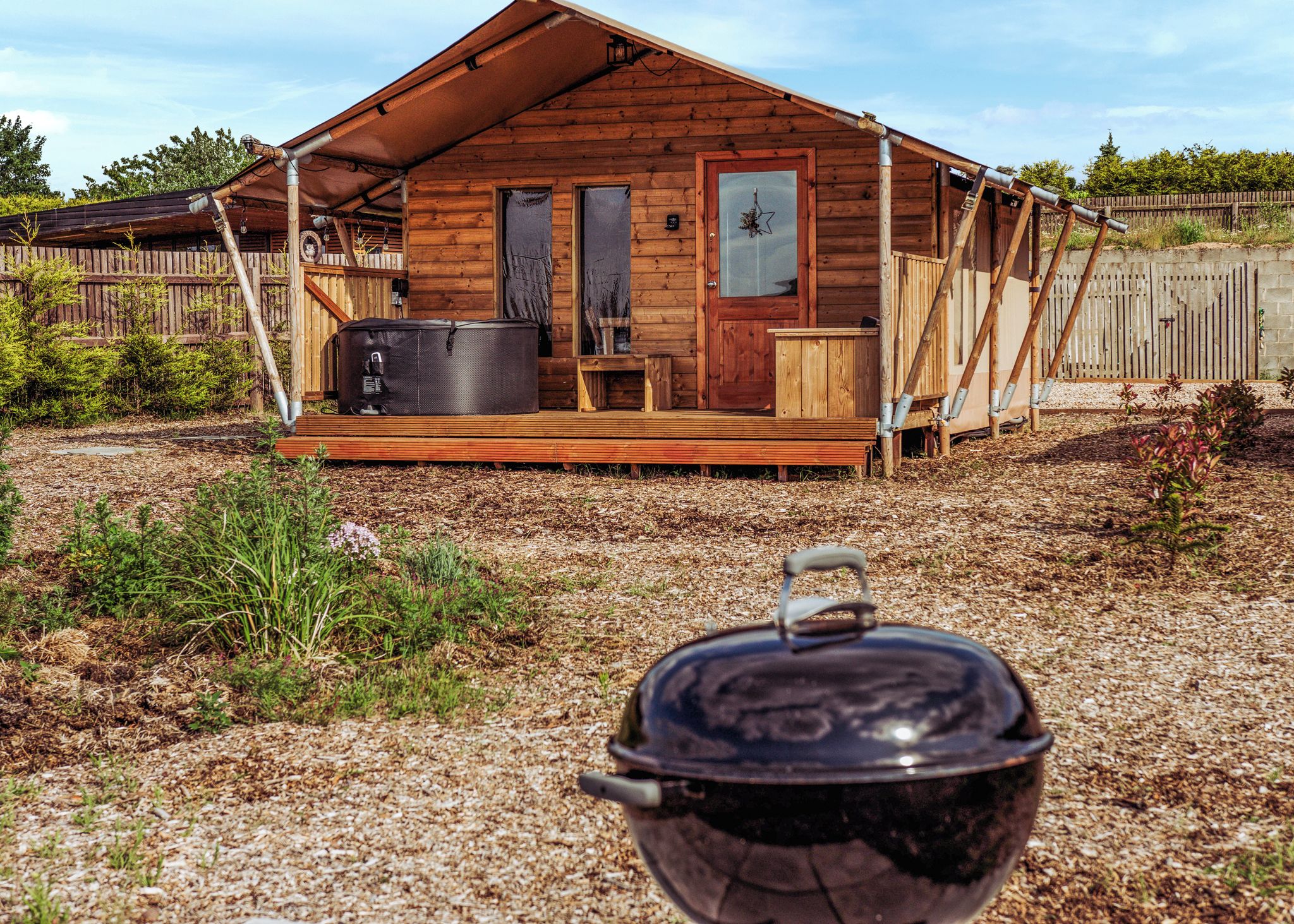 Une cabane en bois avec un porche, un grand pot posé sur le sol et une clôture en arrière-plan.