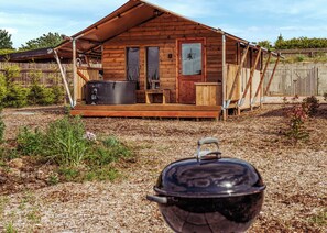 A wooden cabin with a porch, a large pot on the ground, and a fence in the background.