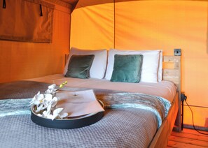 A bed with a headboard, pillows, a blanket, and a tray with flowers and a welcome card.