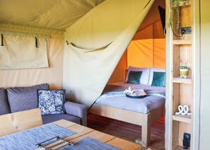A tented accommodation with a bed, a sofa, and a small table.