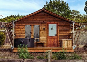 Eine Holzhütte mit Tür, zwei Fenstern und einer kleinen Veranda, sowie einem schwarzen Außenheizer.