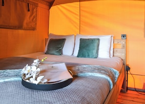 A bed with a headboard, pillows, a blanket, and a tray with flowers and a welcome card.