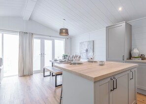 A modern kitchen with a large island, wooden flooring, and a view to the outside. - The Glades 1 Bed Pet Friendly (Westbury)