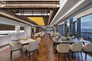 A modern dining area with multiple tables and chairs, large windows, and a view of the cityscape. - Oakwood Residence Foshan (Foshan)