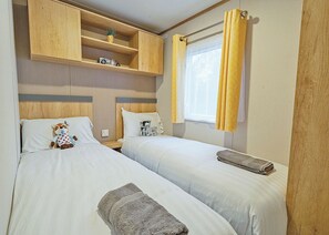 Ein Schlafzimmer mit zwei Betten, Holz-Kopfteilen, einem Regal mit einer Kamera und einem Fenster mit gelben Vorhängen.