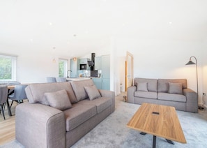 A modern living room with a grey sofa, a wooden coffee table, and a kitchen in the background. - Brand New this year our stunning Lakeland Lodges. (Invermoriston)