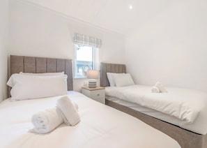 A hotel room with two beds, a nightstand, a lamp, and a window with curtains. - Brand New this year our stunning Lakeland Lodges. (Invermoriston)