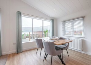 A dining area with a table and chairs, large windows, and a view of the outdoors. - Brand New this year our stunning Lakeland Lodges. (Invermoriston)