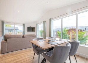 Ein modernes Wohnzimmer mit einer Couch, einem Esstisch mit Stühlen und großen Fenstern mit Blick nach draußen.