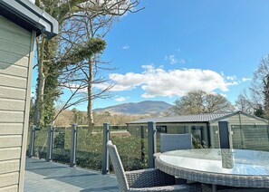 A deck with a wicker chair and a glass table, overlooking a mountainous landscape. - Premium 2 bedroom holiday home with hot tub (Bassenthwaite, near Keswick)