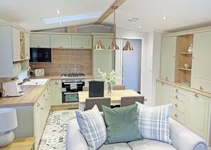 A modern kitchen with a dining area, featuring a central island, pendant lighting, and a built-in oven. - Premium 2 bedroom holiday home with hot tub (Bassenthwaite, near Keswick)
