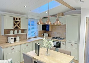 A modern kitchen with a skylight, built-in appliances, and a dining area with a vase of flowers. - Premium 2 bedroom holiday home with hot tub (Bassenthwaite, near Keswick)