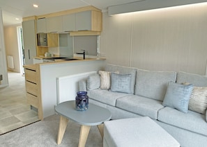 Eine moderne Küchenzeile mit Herd, Backofen und Mikrowelle. Ein graues Sofa mit Kissen und ein kleiner Tisch mit einer Vase sind vorhanden.