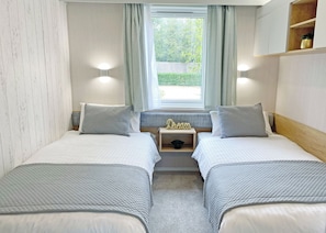 Ein Doppelzimmer mit zwei Betten, einem Fenster mit Vorhängen, einem Nachttisch mit Lampe und einem Regal mit Pflanze.