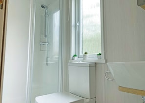 Ein Badezimmer mit Glasdusche, Toilette und Waschbecken unter einem Fenster.