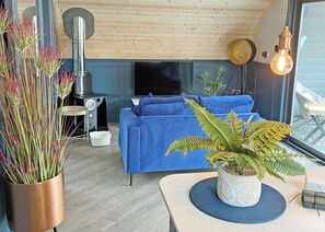 Un salon chaleureux avec un canapé bleu, un plafond en bois, une cheminée et une grande fenêtre.