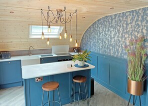 A modern kitchen with a central island, pendant lighting, and a blue accent wall. - Glamping Pod with hot tub - Pet Friendly (Bassenthwaite, near Keswick)