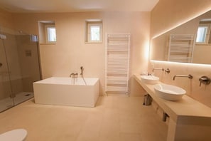 Een moderne badkamer met een badkuip, twee wastafels, een douchecabine met glazen wanden en een grote spiegel.